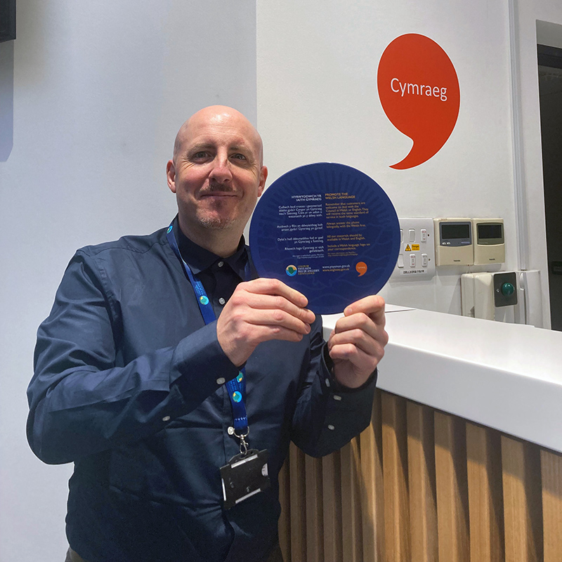 Image of an employee holding a Welsh language promotion flyer